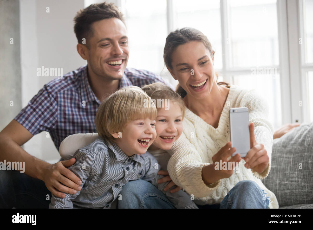 Allegro famiglia con bambini sorridenti tenendo selfie insieme sul telefono, giovane azienda mom smartphone rendendo la foto del figlio e figlia a casa, amare Foto Stock