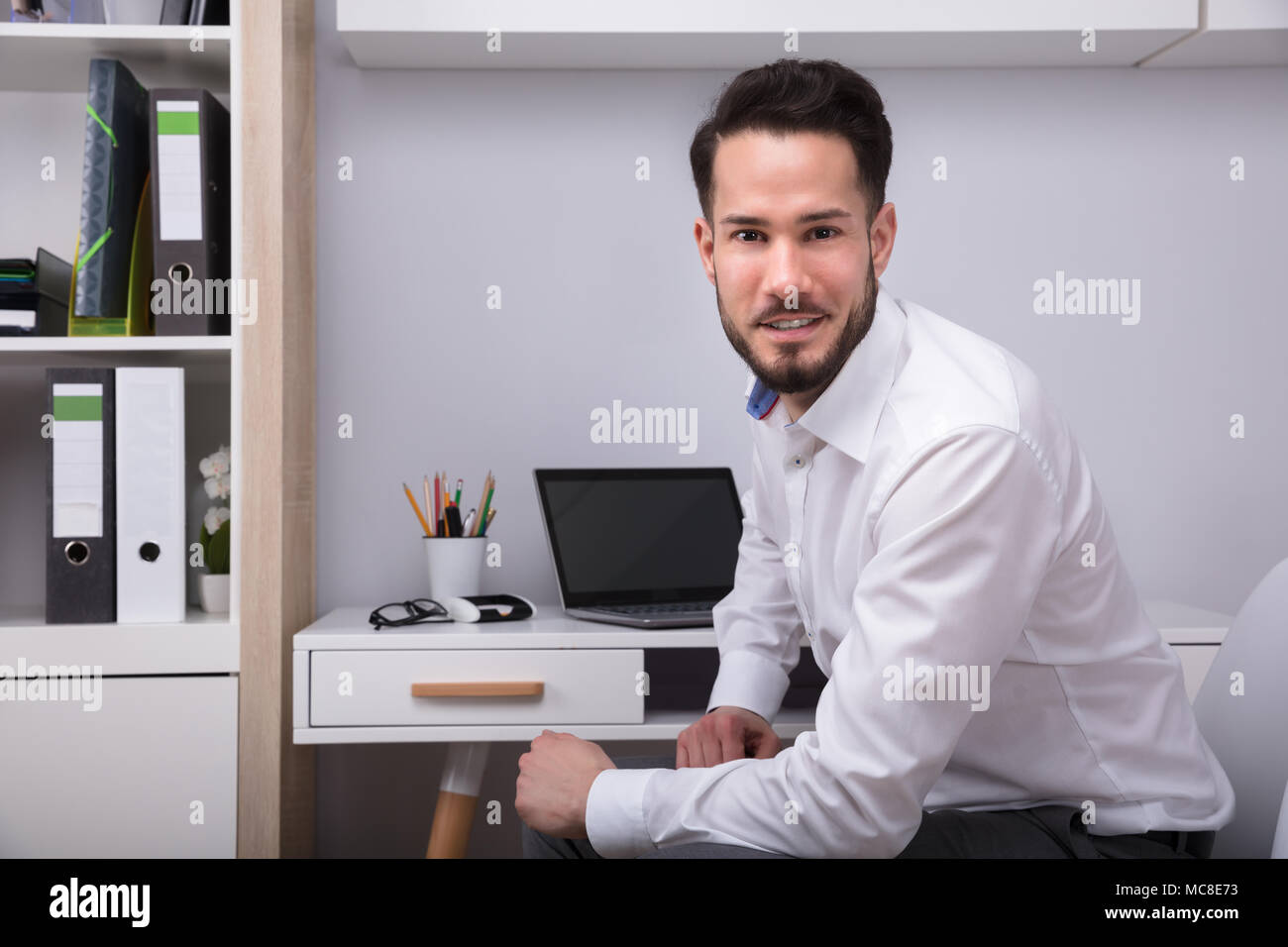 Ritratto di un giovane sorridente imprenditore seduto in ufficio Foto Stock