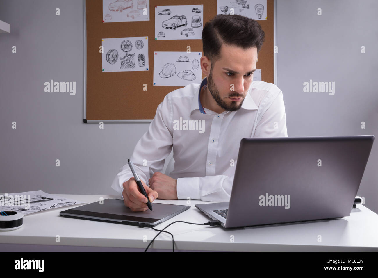 Designer maschio con tavoletta grafica lavorando sul computer portatile Foto Stock