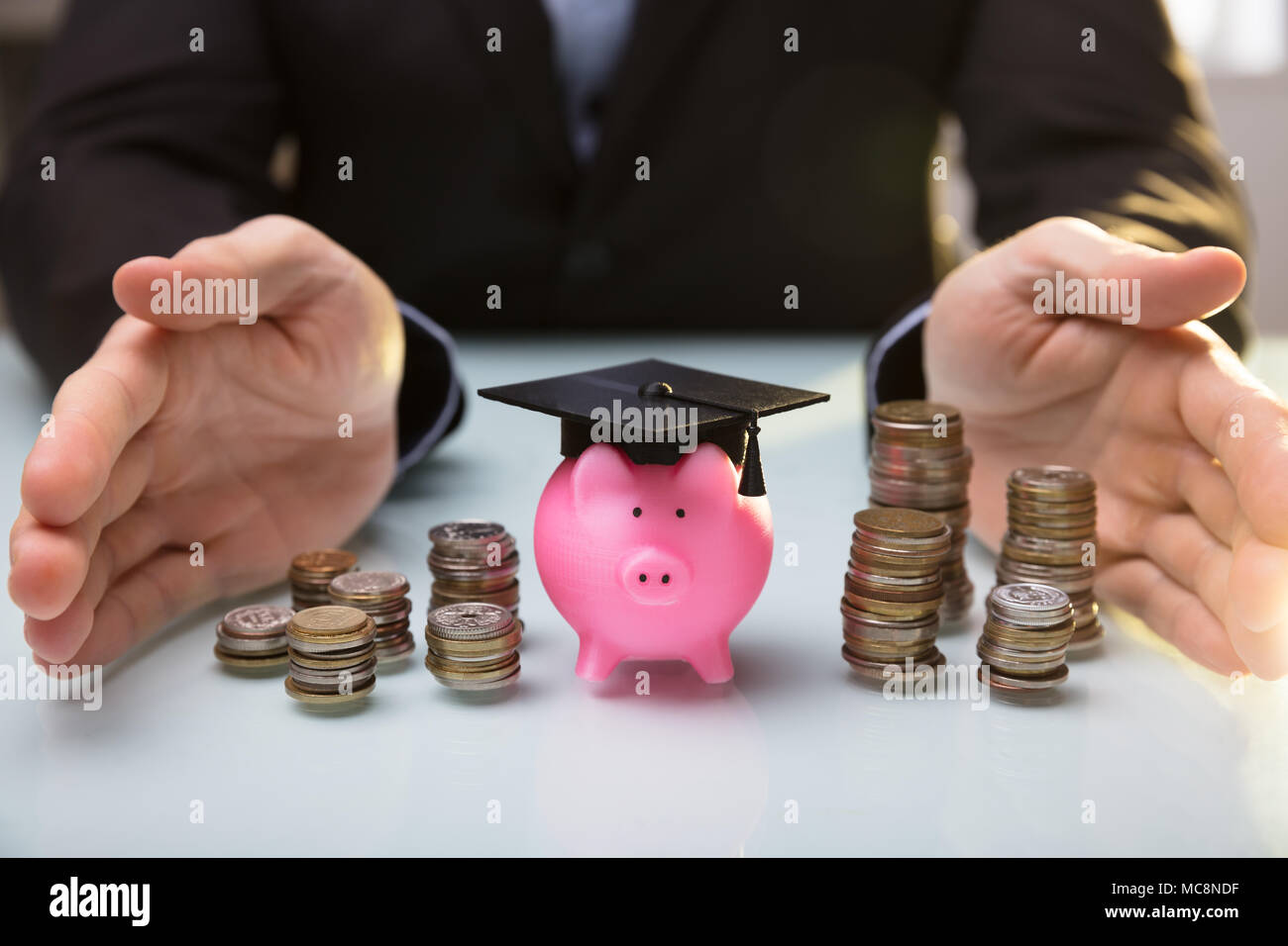 Close-up di un agente di protezione mano Salvadanaio indossando la laurea Hat e monete impilate Foto Stock