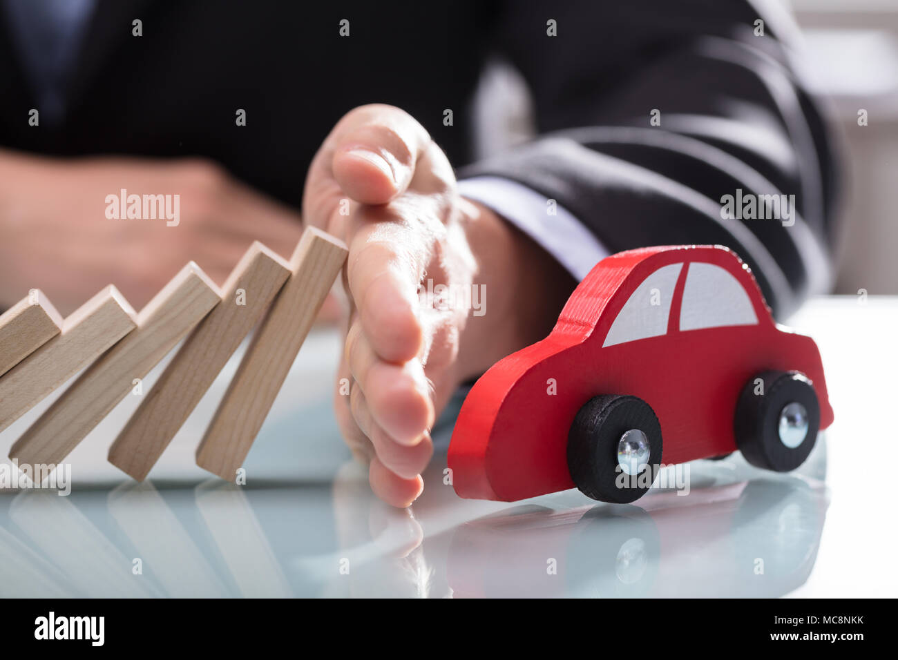 Close-up di un imprenditore la mano arrestando i blocchi di legno dalla caduta su auto rossa sulla scrivania Foto Stock