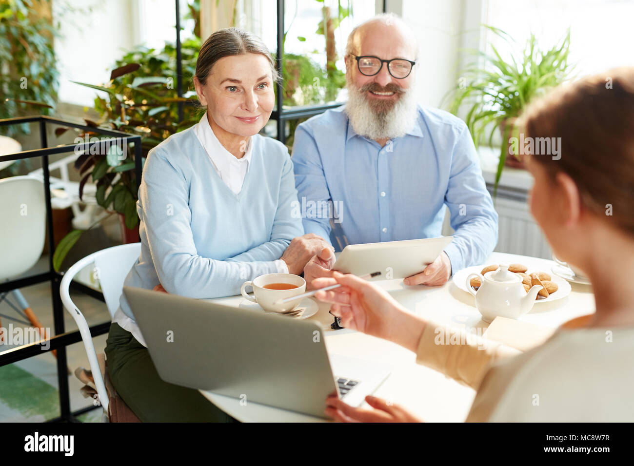 Agente moderno puntando al display del notebook mentre spiegare i dati di coppia senior alla riunione Foto Stock
