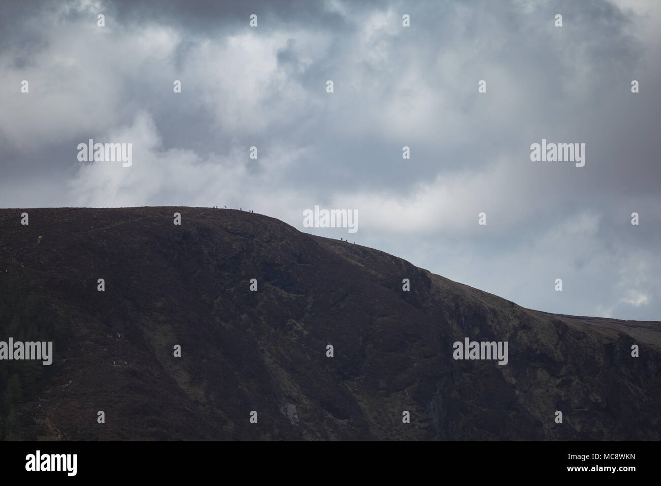 La gente sul picco della Spinc ridge che si affacciano sulla spettacolare Valle di Glendalough in Wicklow Parco naturale in Irlanda. Nuvole drammatico. Foto Stock