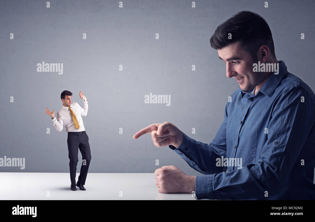 Giovane imprenditore professionale essendo arrabbiato con un altro imprenditore in miniatura di fronte a uno sfondo grigio Foto Stock