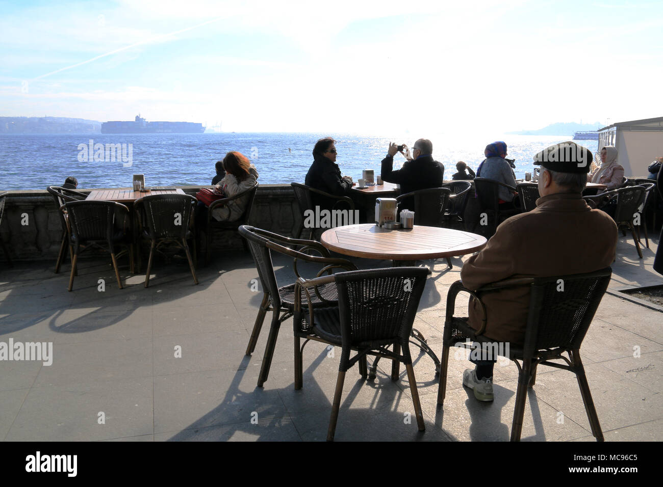 Contenitore grande nave di navigare attraverso il Bosforo, visto da una graziosa caffetteria al bordo dell'acqua ad Istanbul in Turchia Foto Stock