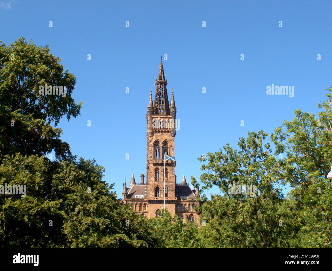 L'Università di Glasgow clock tower vista dal kelvingrove park con bandiera scozzese si intraversa sul pennone Foto Stock