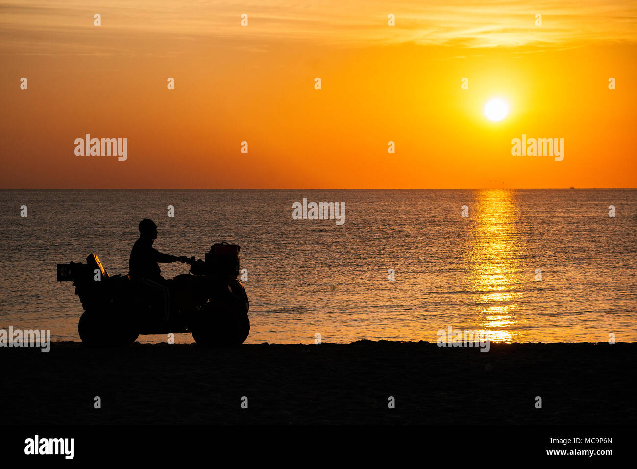 Un ATV si staglia al sole che sorge su una spiaggia della Florida con un luminoso e colorato cielo giallo e oceano come sfondo. Copia Spazio Foto Stock