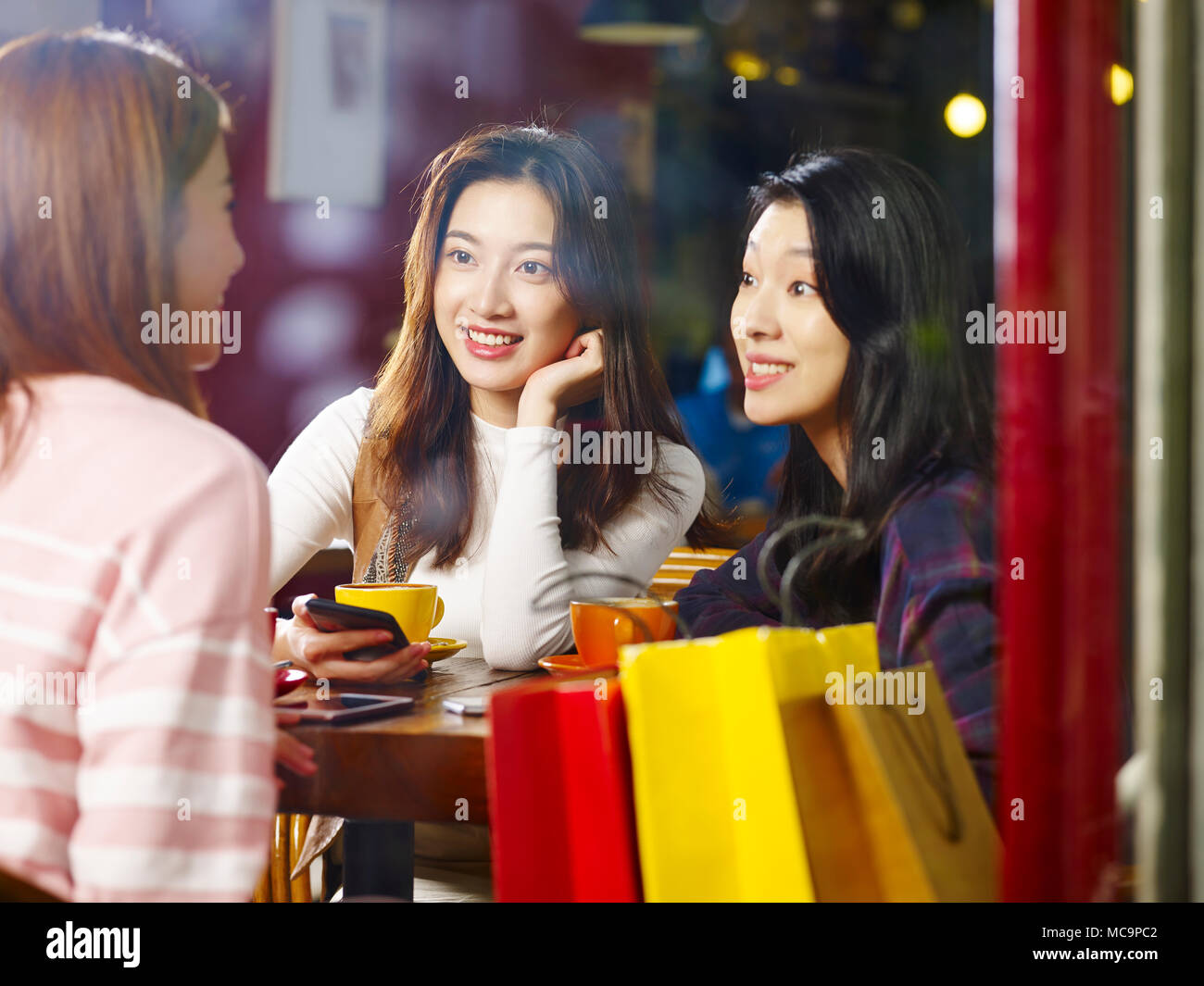 Tre felice giovane e belle donne asiatiche seduta a tavola in chat parlando in negozio di caffè o tè casa, shot attraverso il vetro di una finestra. Foto Stock