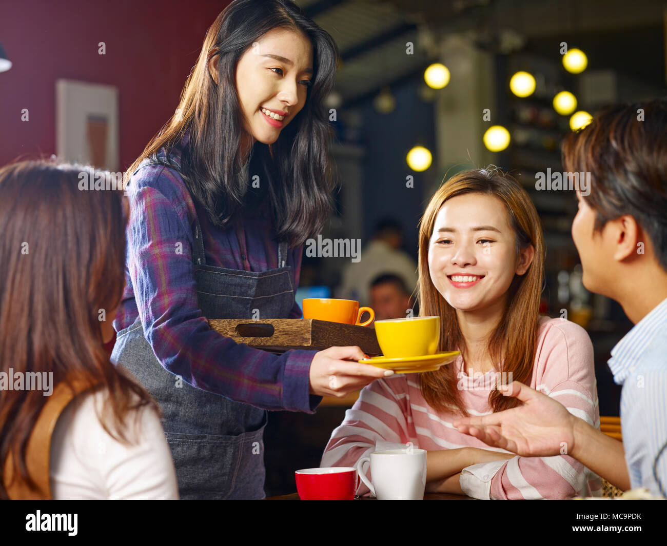 Giovani asiatici sorridente cameriera che serve caffè ai clienti. Foto Stock