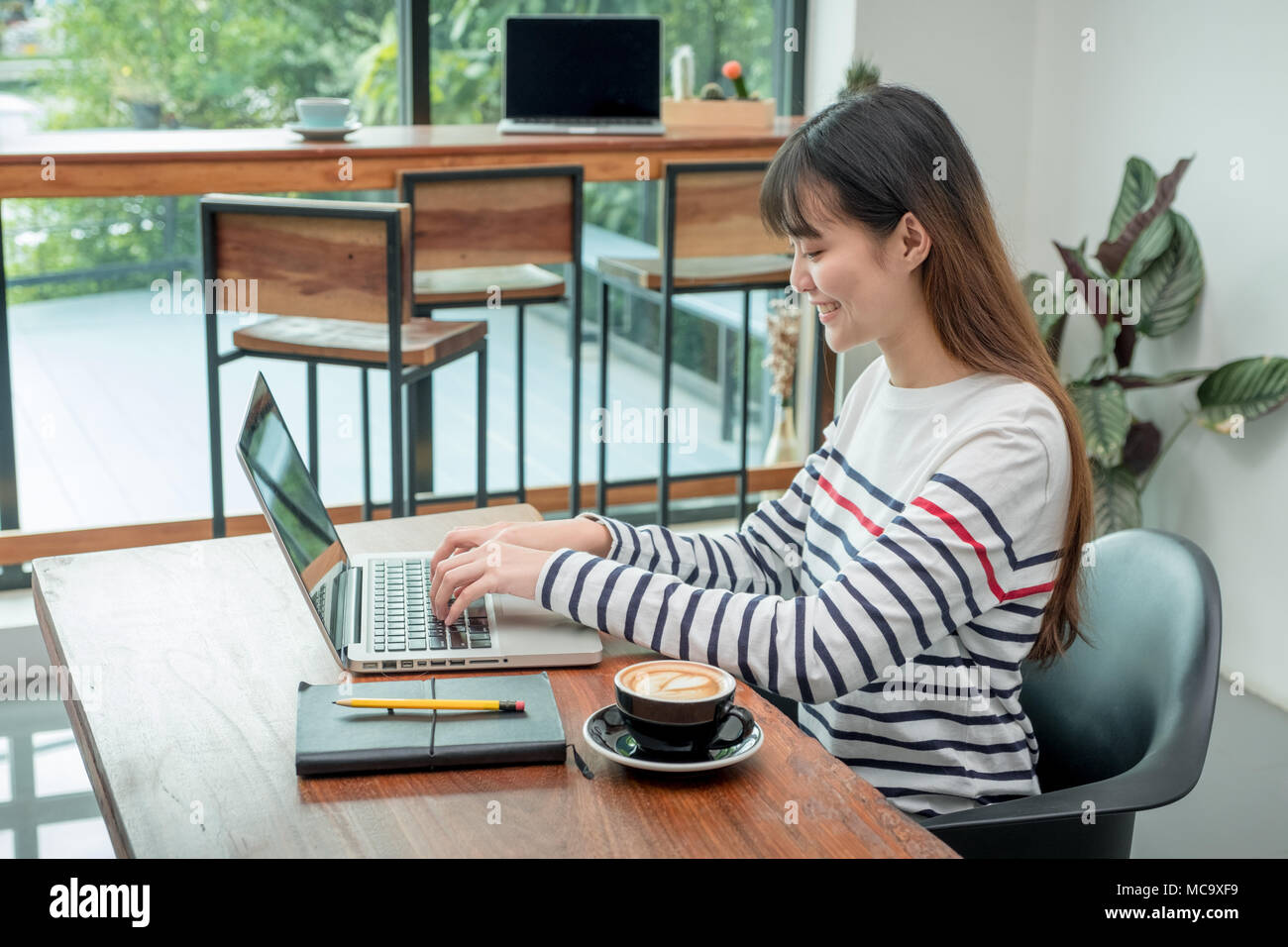 Felice donna asiatica utilizzando il computer portatile mentre si lavora vicino alla finestra al ristorante cafe,Digital co e spazio di lavoro stile di vita.influencer blogger review.w Foto Stock