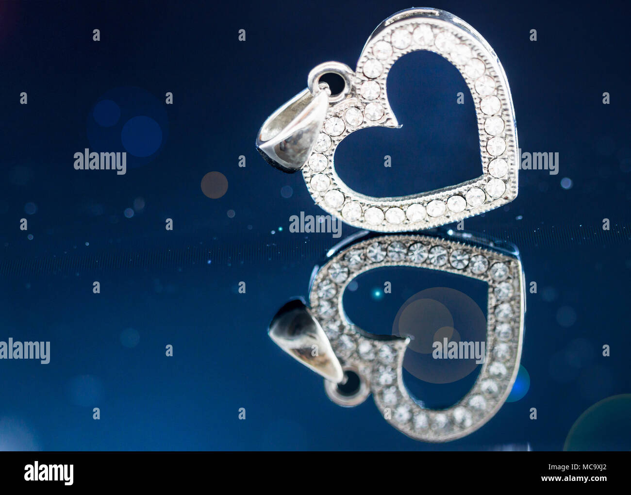 Argento diamante cuore pendente in blu scuro dello sfondo con la riflessione e il bokeh con copia spazio o spazio per immissione di testo. Foto Stock