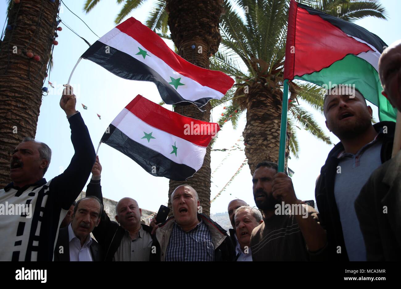 (180414) -- NABLUS, Aprile 14, 2018 (Xinhua) -- dimostranti palestinesi wave siriana e bandiere palestinese durante una manifestazione di protesta a seguito di una ondata di Stati Uniti, inglesi e francesi di scioperi militare sulla Siria, in Cisgiordania città di Nablus, il 14 aprile 2018. (Xinhua/Ayman Nobani) (SWT) Foto Stock