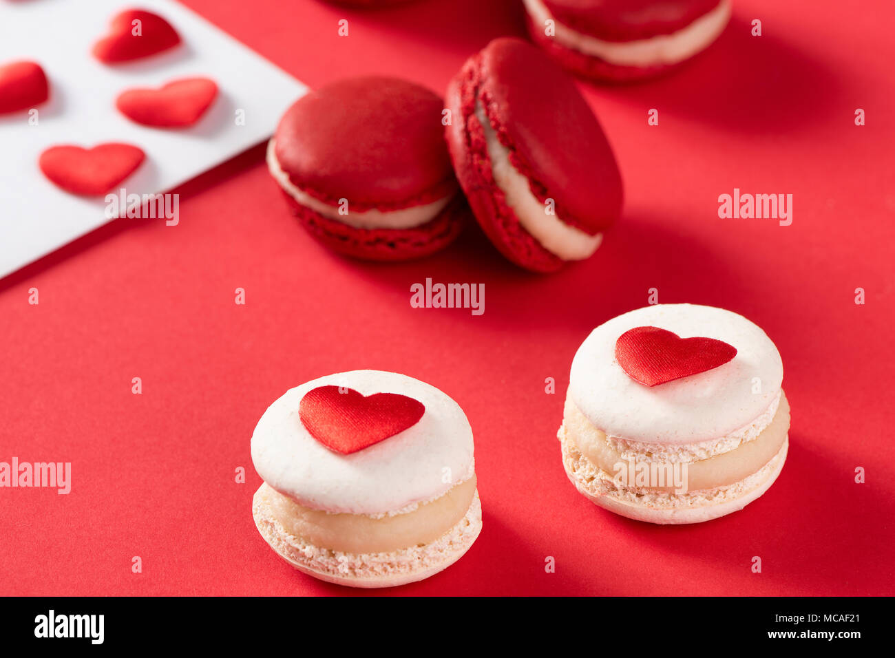 Cuori rossi con francese macaron rosso su sfondo rosso, il concetto di amore Foto Stock