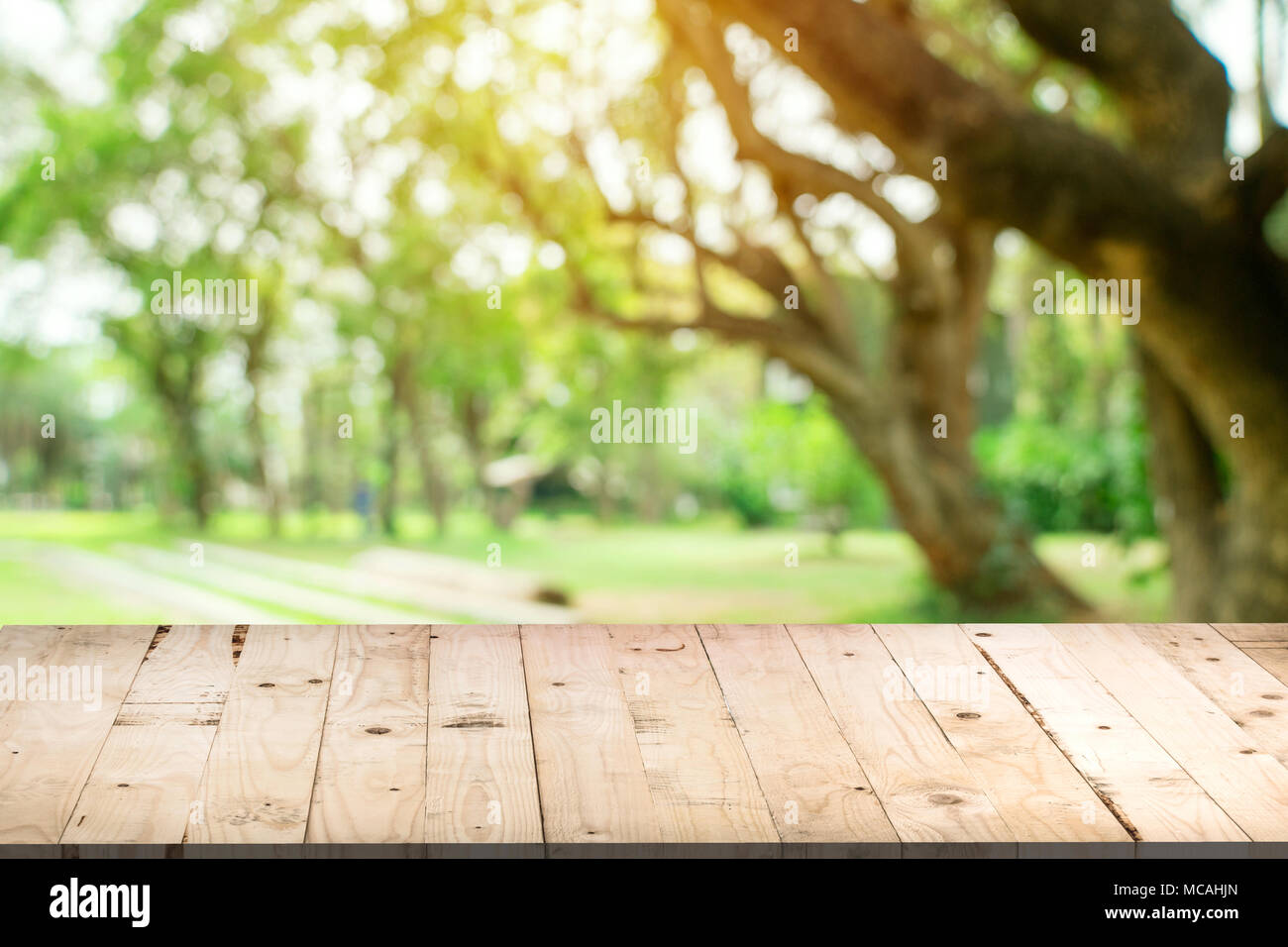 Svuotare tavolo in legno e defocalizzata bokeh di fondo e la sfocatura sullo sfondo di un giardino di alberi nella luce solare, display montage per prodotto. Foto Stock