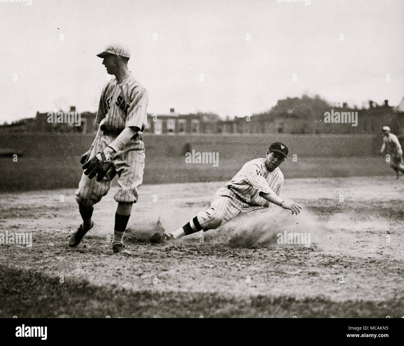 Washington senatori' Bucky Harris scorrevole, come egli riesca a ruba la terza base nel settimo inning di una partita di baseball contro il Boston Red Sox; terzo baseman Joe Dugan orologi la sfera rotolare verso sinistra il campo dopo un tiro selvaggio. Senatori shut-out Red Sox 10-0 Foto Stock