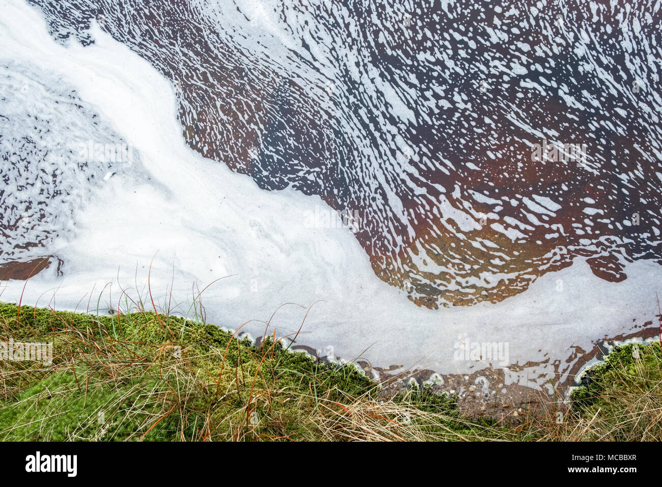 Con flusso di schiuma sulla superficie dell'acqua passando da una banca di erba e muschio, Kinder Scout, Derbyshire, Peak District, England, Regno Unito Foto Stock