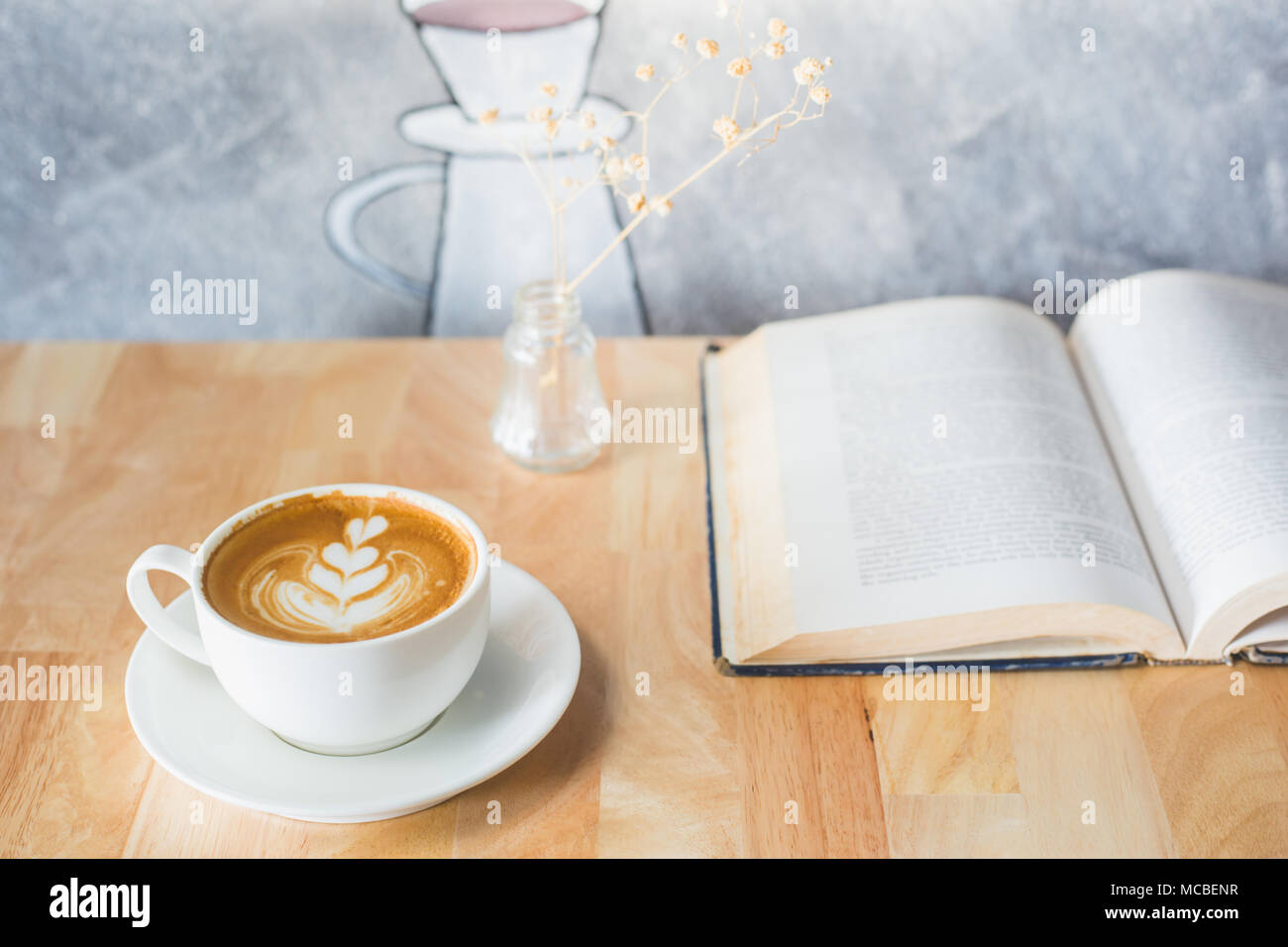 Caffè latte a forma di cuore con libro sul tavolo Foto Stock