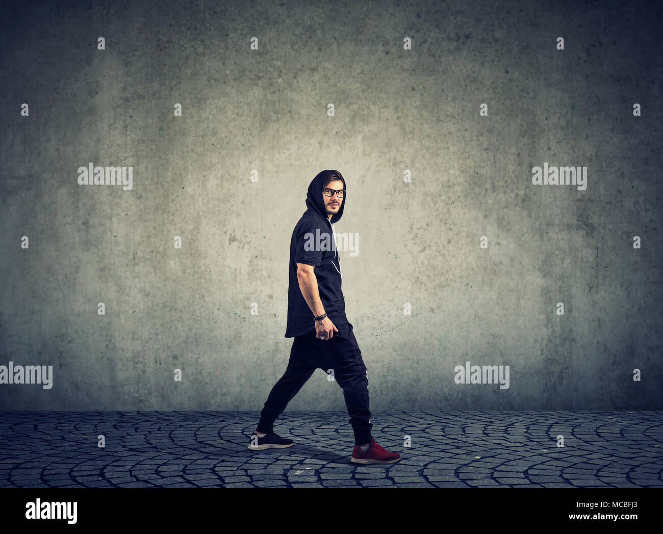 Vista laterale di stile hip-hop ballerino in bicchieri a piedi in sportswear guardando la fotocamera. Foto Stock