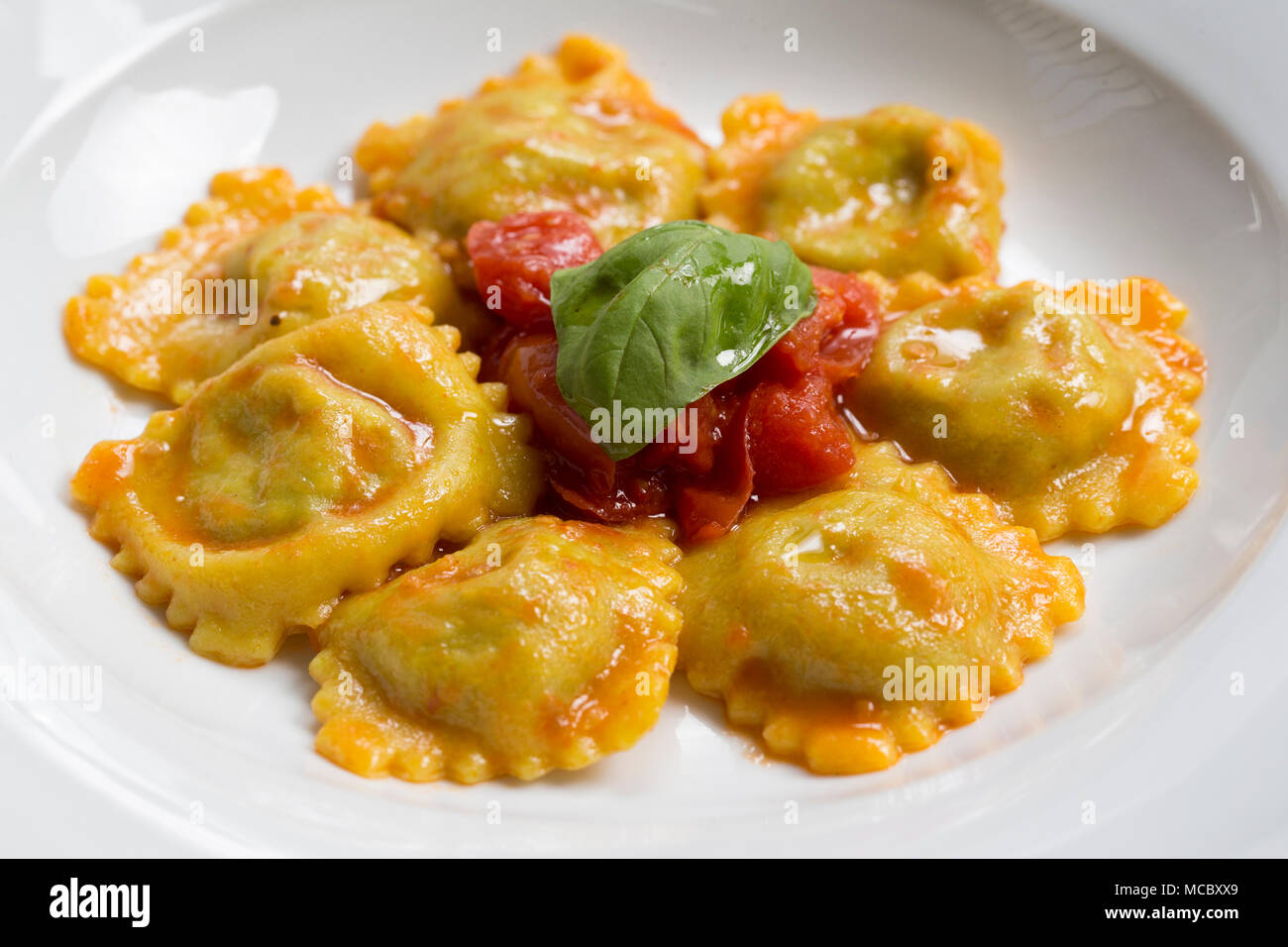 Scatto frontale di un tipico piatto italiano, un piatto di ravioli con il ripieno di verdure e salsa di pomodoro e basilico sulla parte superiore Foto Stock