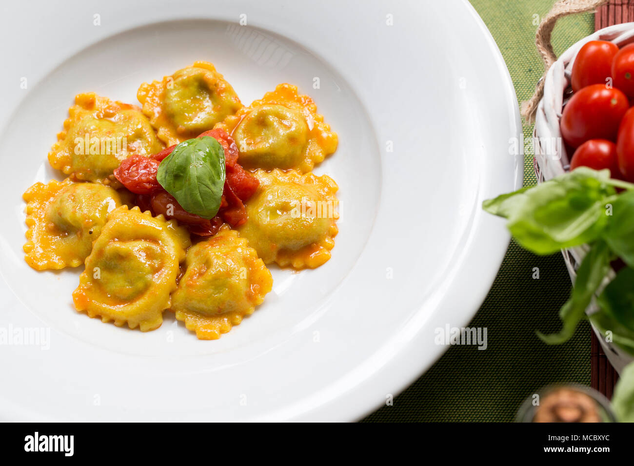 Una piastra di italian pasta ripiena, ravioli con salsa di pomodoro fresco, le foglie di basilico e olio di oliva con soggetti e concentrarsi sulla sinistra su un tavolo verde panno Foto Stock