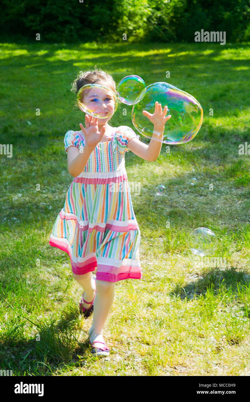 Bambina arcobaleno di cattura bolle di sapone in estate park. Foto Stock