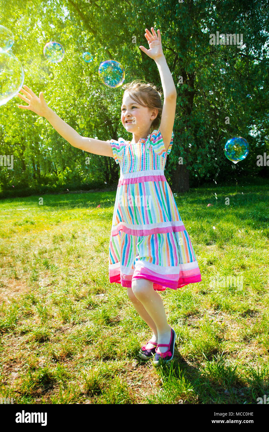 Bambina arcobaleno di cattura bolle di sapone in estate park. Foto Stock