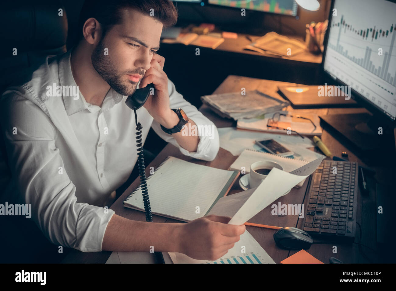 Commerciante di parlare al cliente sui tassi di cambio mentre si lavora fino a tardi in ufficio, analista finanziario avente la conversazione telefonica chiamando il cliente, stock br Foto Stock