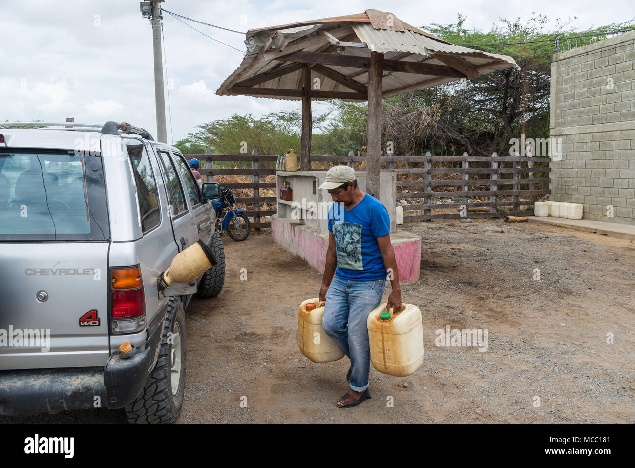 Un uomo porta due brocche di benzina per riempire un'auto in una zona rurale petro station. La Colombia, Sud America. Foto Stock