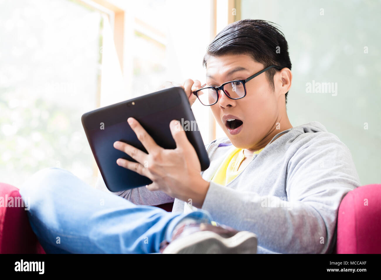 Giovane uomo asiatico sorpreso da online informazioni visualizzate su un tablet PC Foto Stock