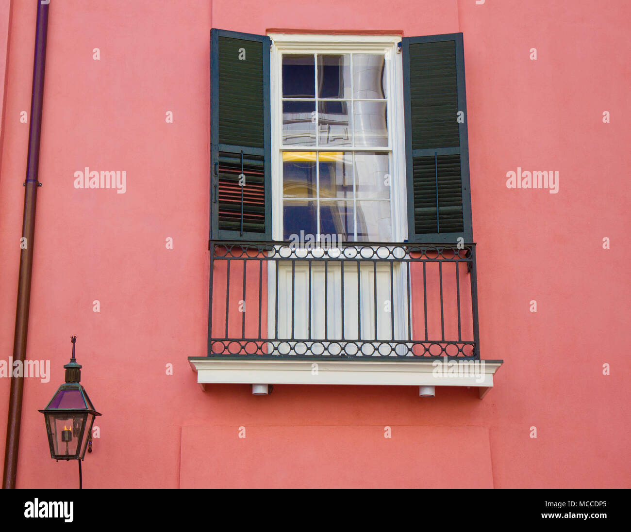 Con finestra con persiane verdi sul salmone colorato casa nel quartiere francese, New Orleans, in Louisiana. Piccolo cast balcone in ferro finestra sottostante, lampada a gas Foto Stock