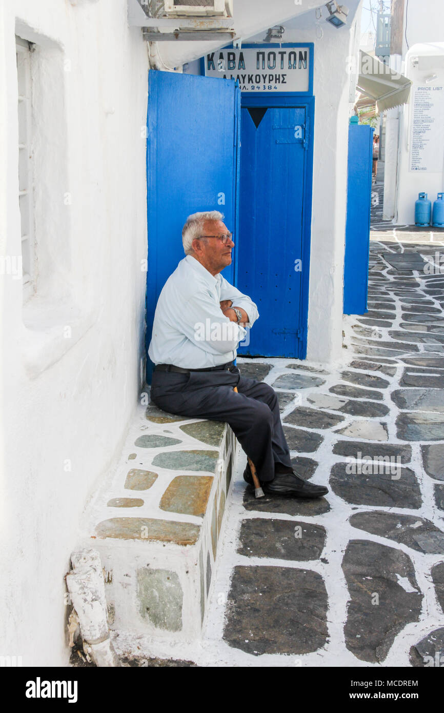 Uomo seduto sul sedile in pietra, Chora, a Mykonos, Grecia Foto Stock