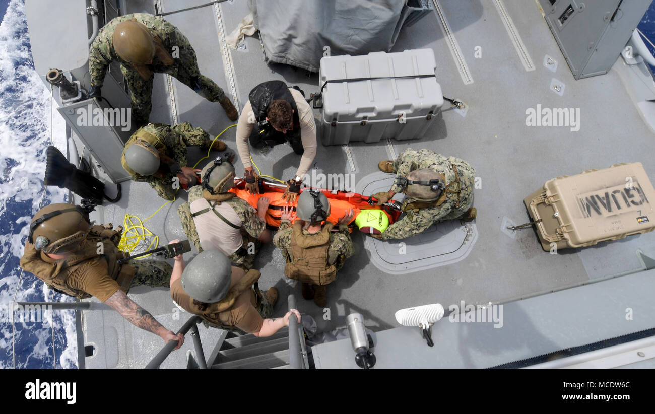 Costiera squadrone fluviale (CRS) 4, det. Guam e elicottero mare squadrone di combattimento (HSC) 25 marinai di caricamento di una ricerca e di salvataggio (SAR) falsa su una barella a bordo di un marchio vi imbarcazione di pattuglia durante un giunto SAR esercizio con U.S. Coast Guard Settore Guam, 23 febbraio, 2018. CRS-4, assegnato a Costiera gruppo fluviale 1, det. Guam, è in grado di condurre le operazioni di sicurezza marittima nell intero spettro del Naval, giunto e operazioni combinate. Inoltre, esso fornisce funzionalità aggiuntive di sicurezza del porto, avviato la sicurezza, e il teatro di cooperazione per la sicurezza intorno all'U.S. 7 flotta area di operazioni. (U.S. Na Foto Stock