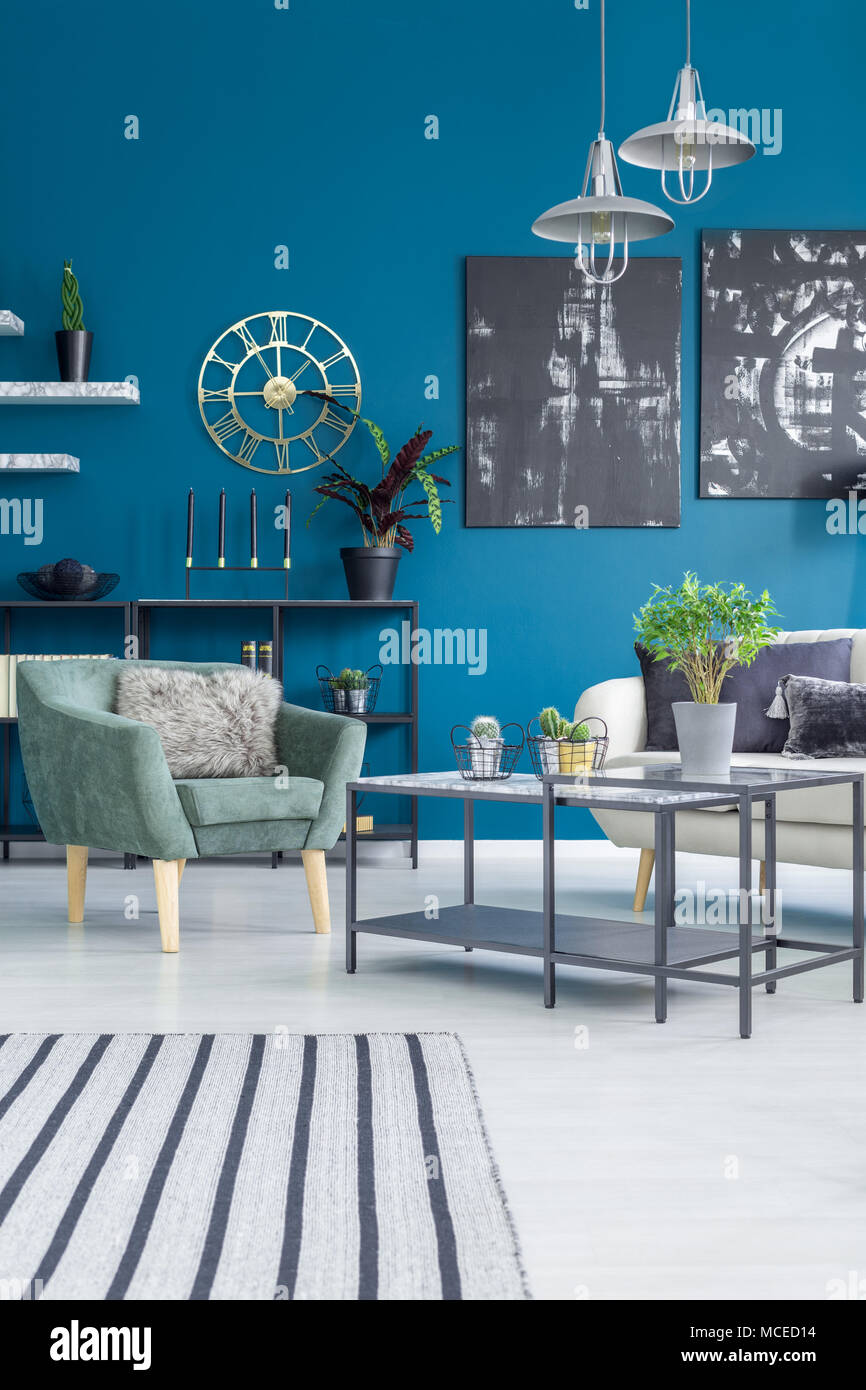 Poltrona verde accanto a un tavolo con impianto contro la parete blu con oro Orologio rotondo in living room interior Foto Stock