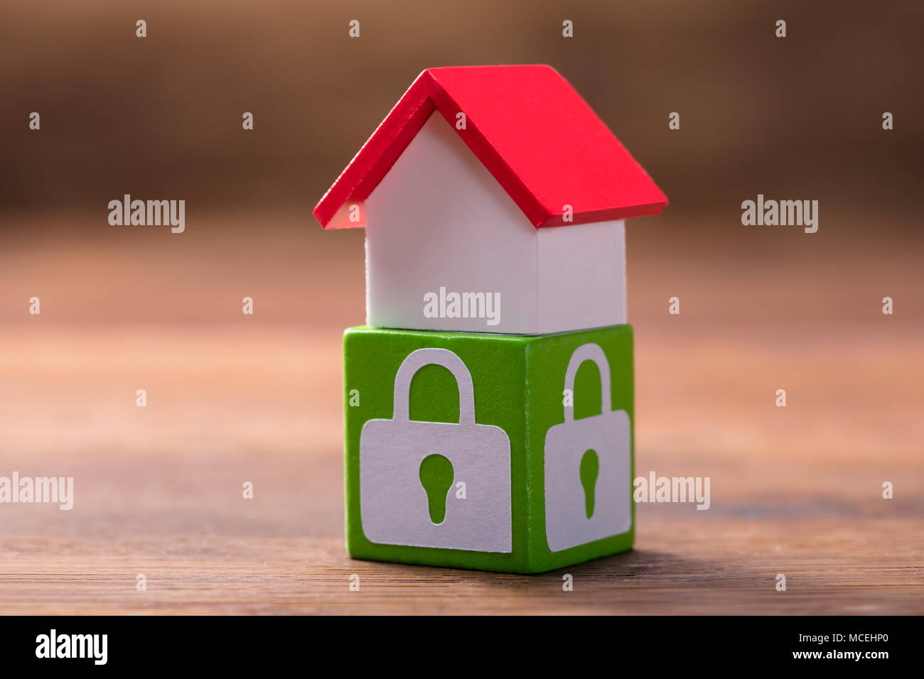 Modello di casa con il tetto rosso sul blocco verde con simboli di bloccaggio sopra la scrivania in legno Foto Stock