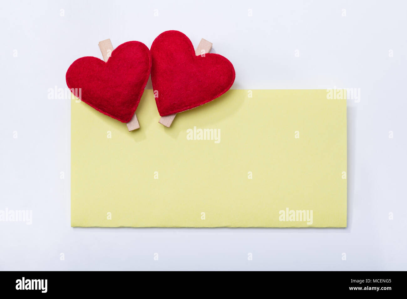 Vista in elevazione dello sbozzato Scheda gialla con due cuore Clothespins su sfondo bianco Foto Stock