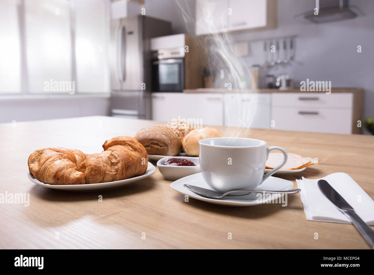 Close-up di croissant e la tazza di caffè caldo sulla scrivania in legno Foto Stock