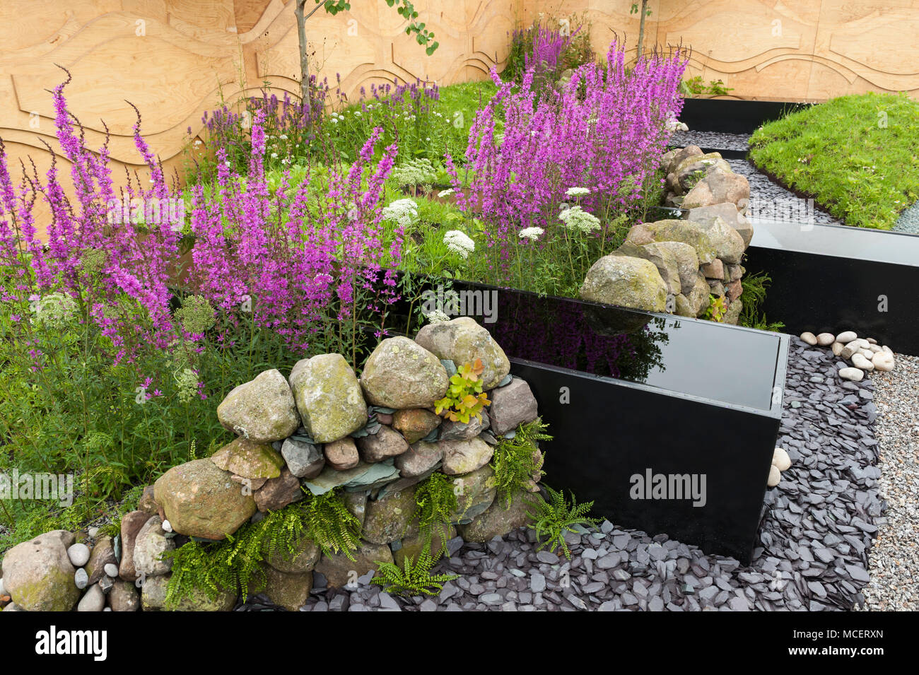 Acciaio acqua trogoli, muro di pietra, recinzione in tela, fiori colorati e ghiaia - 'acque chiare Rising l' mostrano il giardino - RHS Flower Show, Tatton Park, England, Regno Unito Foto Stock