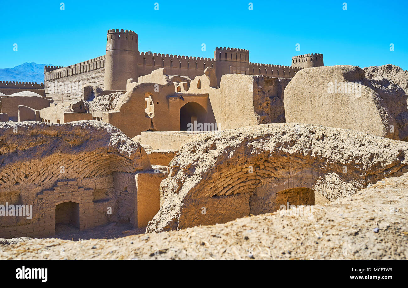 Rovine di antichi edifici in sito archeologico e le massicce mura e torri del castello di Rayen sullo sfondo, l'Iran. Foto Stock