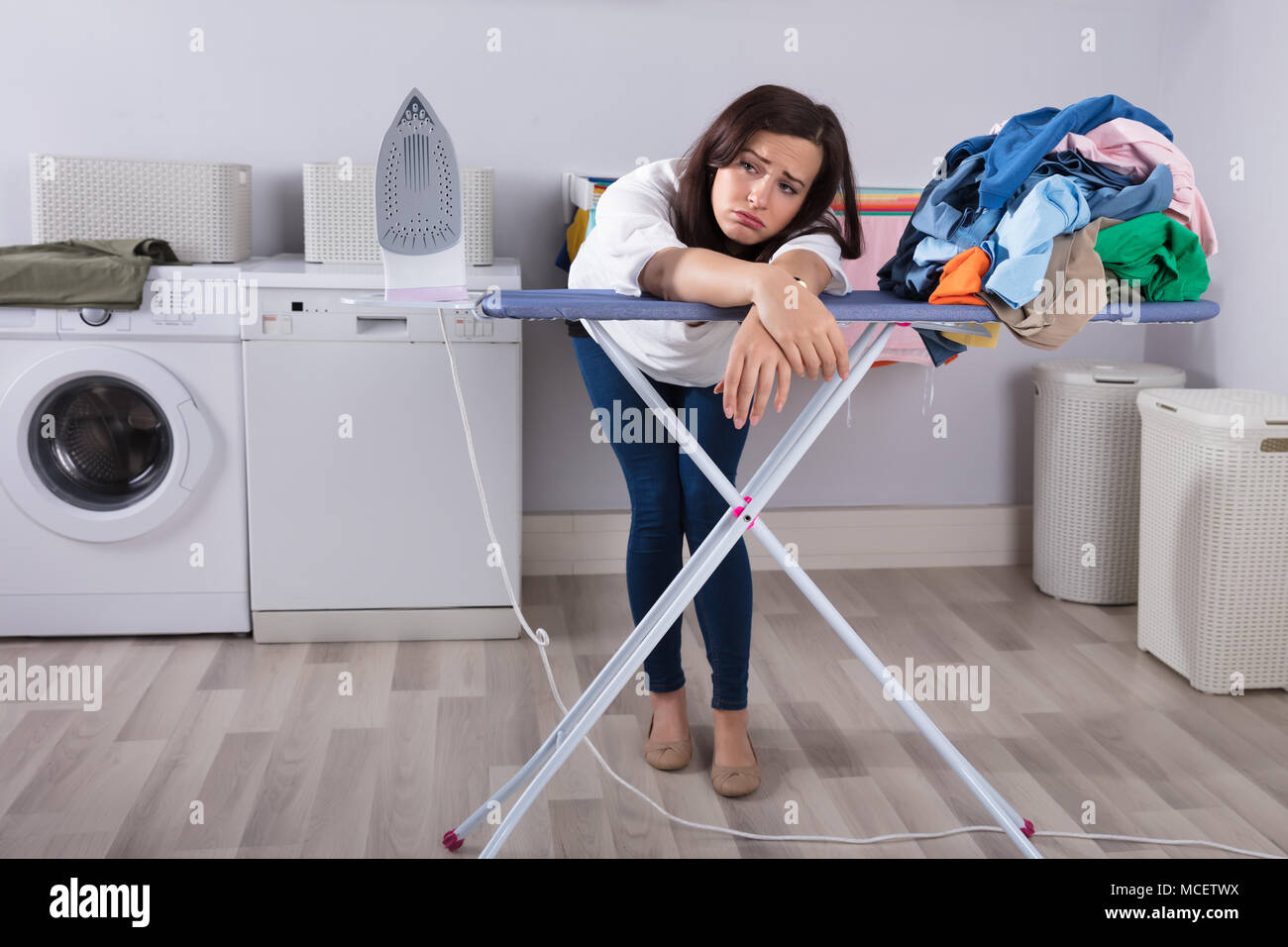 Donna infelice appoggiata sulla tavola da stiro accanto al mucchio di vestiti Foto Stock