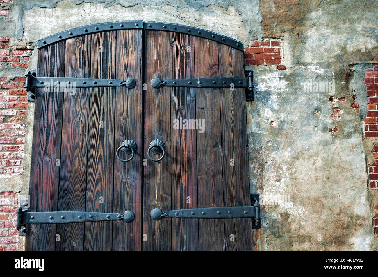 Close up di un pesante impianto di legno a doppia porta con cerniere di ferro e maniglie,chiudendo l'ingresso in un vecchio edificio in mattoni. Foto Stock
