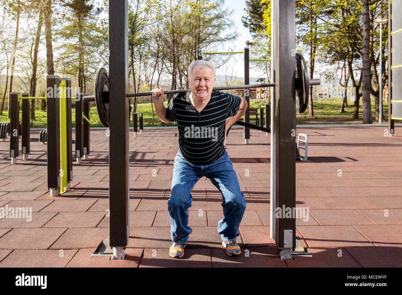 Uomo anziano riscaldamento fino alla barra pesi nel parco fitness (all'aperto Palestra) Foto Stock
