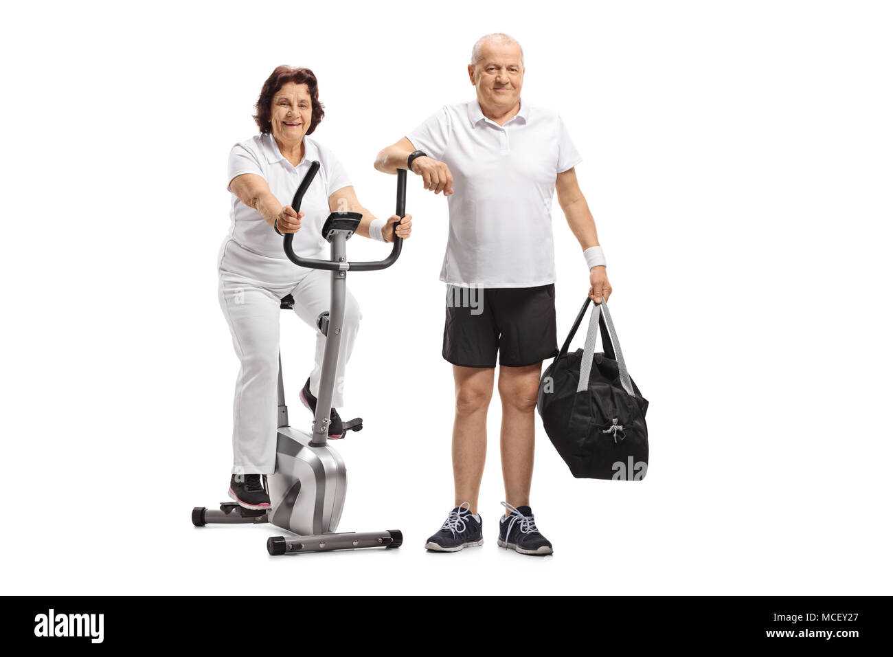 Donna matura su una bicicletta stazionaria e un uomo maturo con una borsa sportiva isolata su sfondo bianco Foto Stock