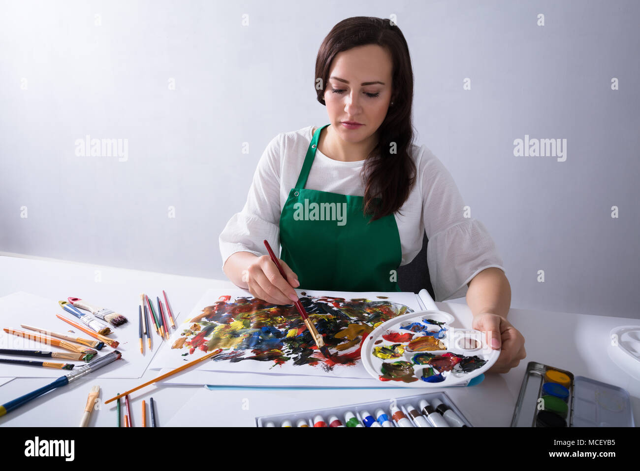Close-up di un artista femminile la mano che tiene la palette di vernice mentre la pittura su tela carta Foto Stock
