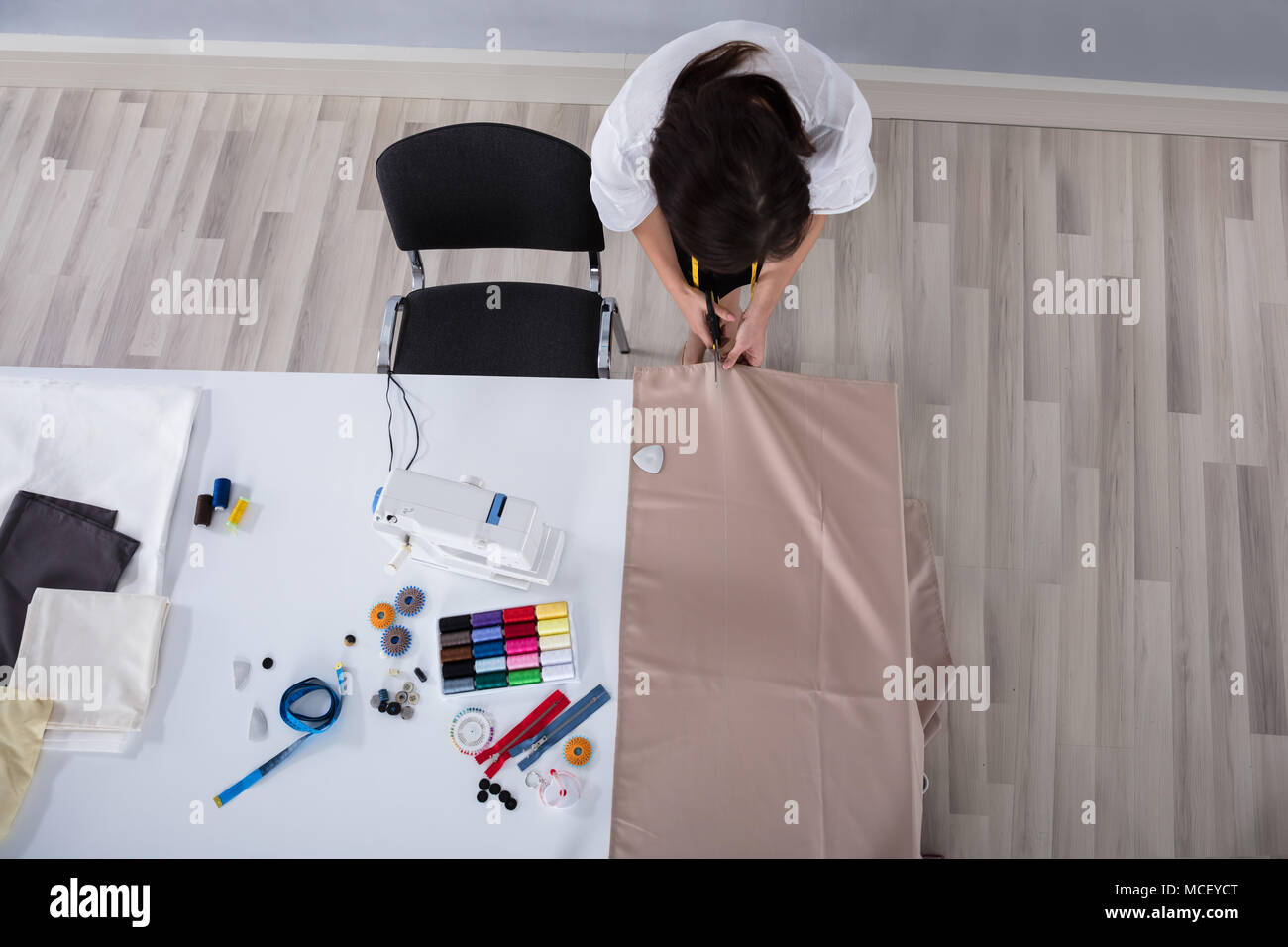 Femmina giovane stilista di moda panno di taglio con le forbici sulla scrivania in Studio Foto Stock