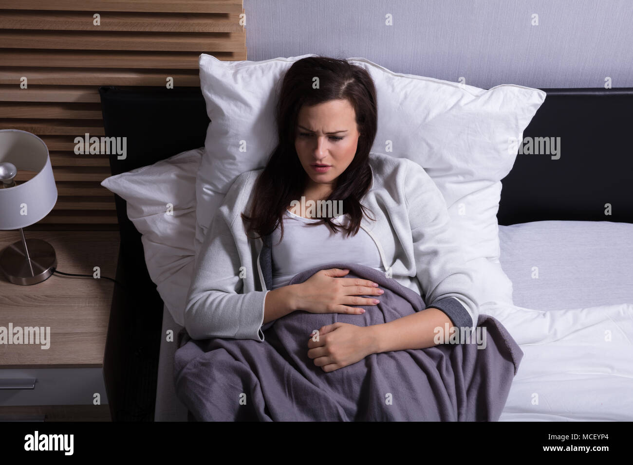 Angolo di Alta Vista di una giovane donna sdraiata sul letto che soffrono di dolori di stomaco Foto Stock