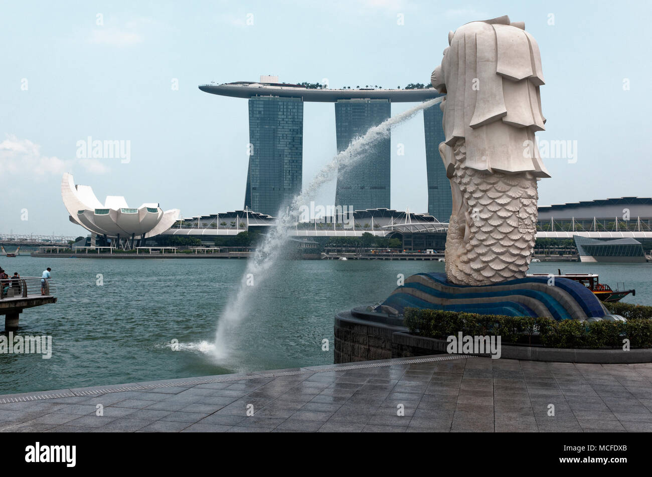 L'acqua che scorre il beccuccio del landmark Singapore Merlion con Marina Bay Sands in hotel in background. Foto Stock