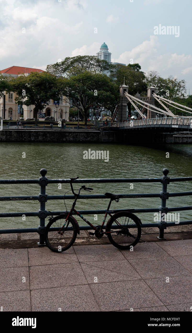 Bicicletta appoggiata sulla ringhiera dal fiume Singapore e Cavanagh Bridge Foto Stock