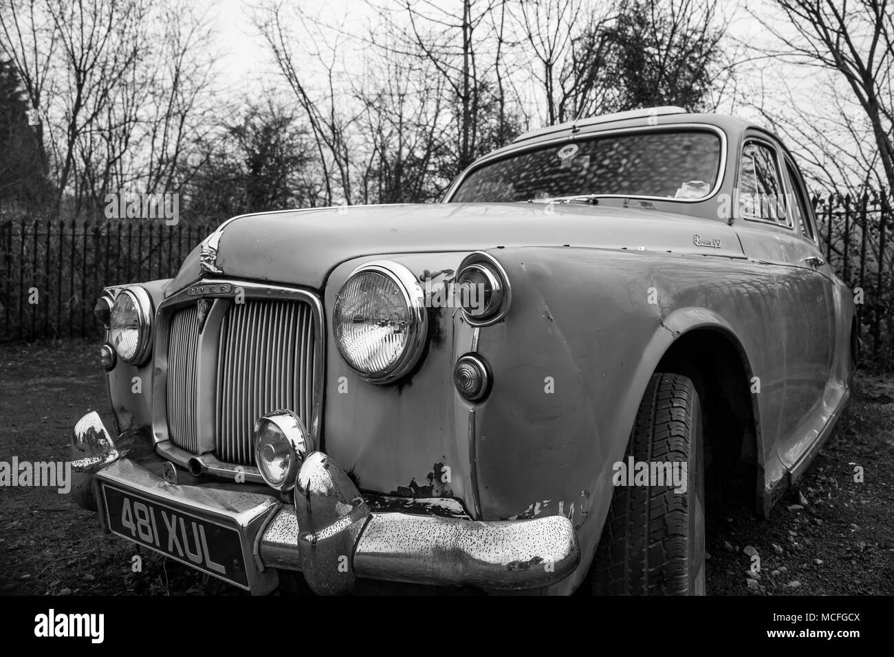 In bianco e nero in prossimità di un Rover P90 che ha visto tempi migliori e ora è una reliquia abbandonata in pensione, da soli in un deserto parcheggio auto. Foto Stock