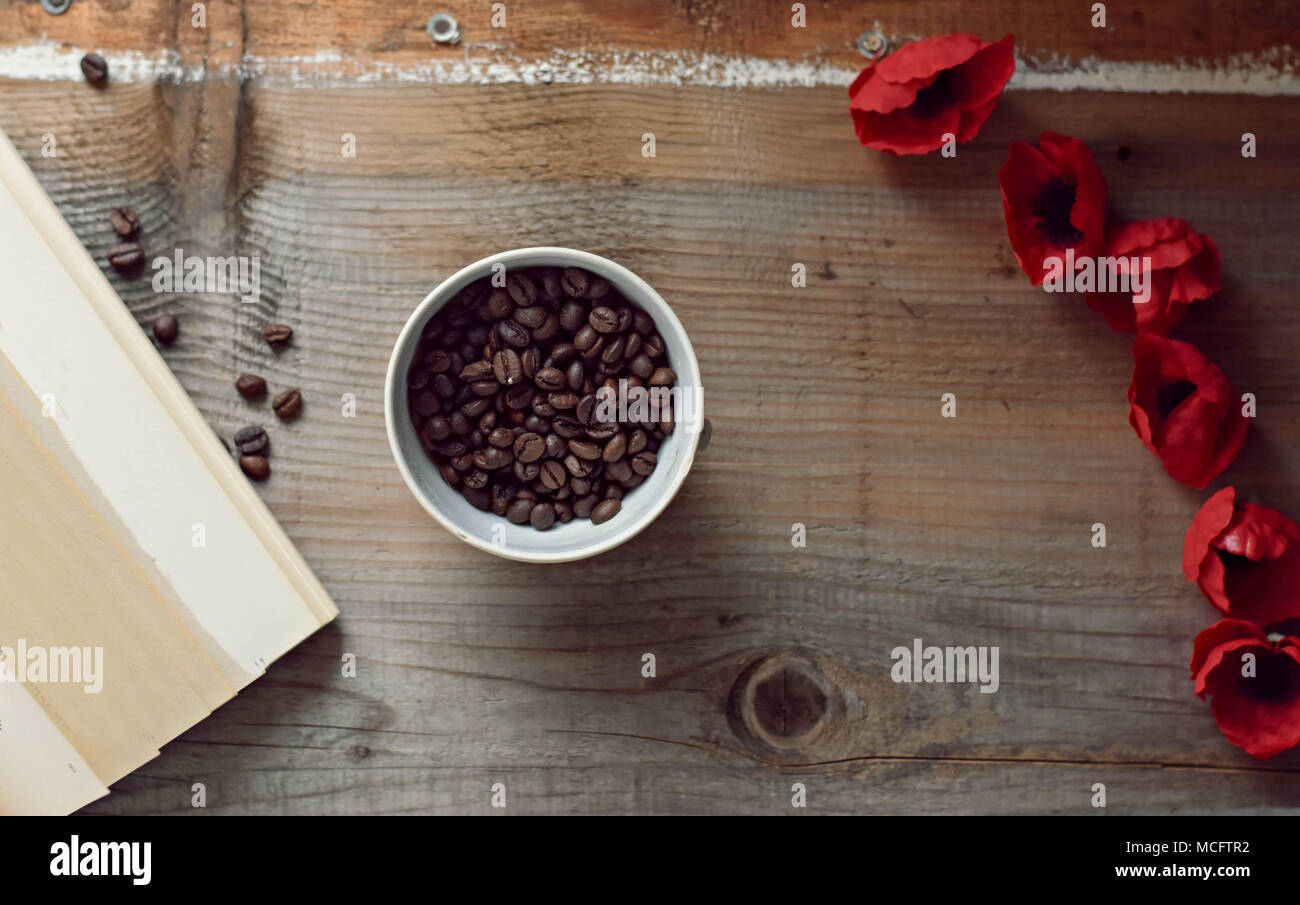 I chicchi di caffè, il vecchio libro e fiori di colore rosso su sfondo di legno Foto Stock