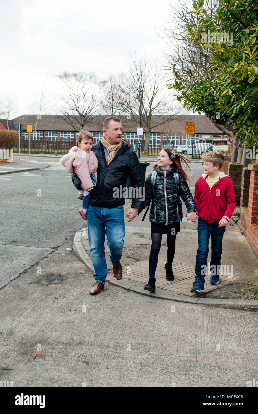 Uomo maturo ha appena prelevato la sua figlia dalla scuola con altri suoi due figli. Essi stanno parlando di come essi a casa a piedi insieme. Foto Stock
